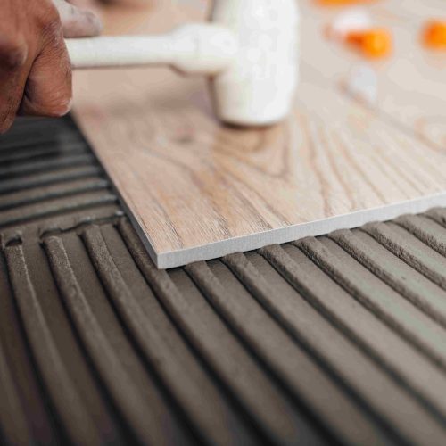Flooring and tiling. Professional tiler placing floor tiles on a Flooring and tiling. Professional tiler placing floor tiles on adhesive surface.
